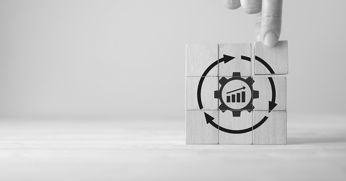 A hand placing teh final cube to a square made up of wooden blocks that show the image of a cog surrounded by a circle of arrows 